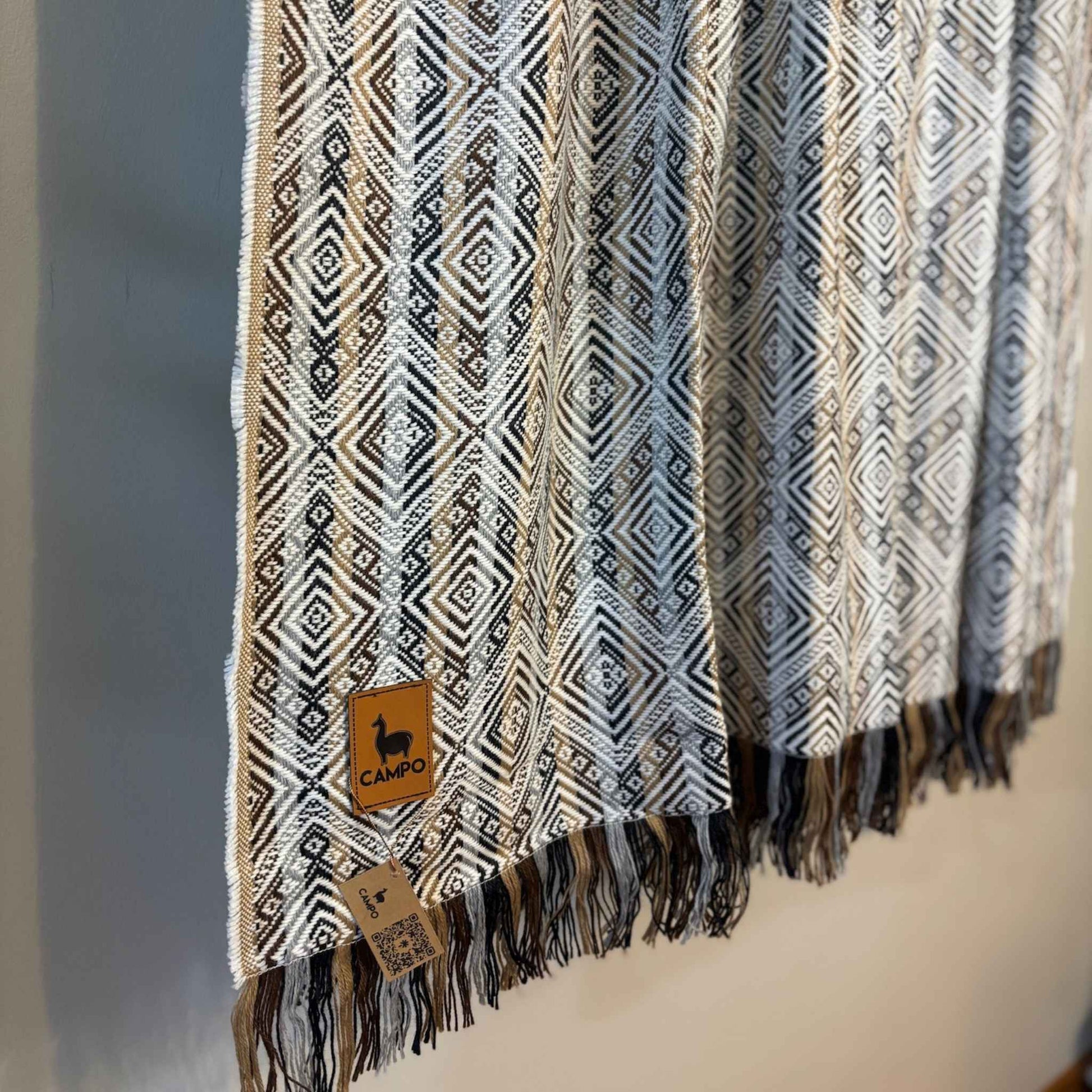 White natural patterned scarf with fringes and a visible brand tag on a neutral background