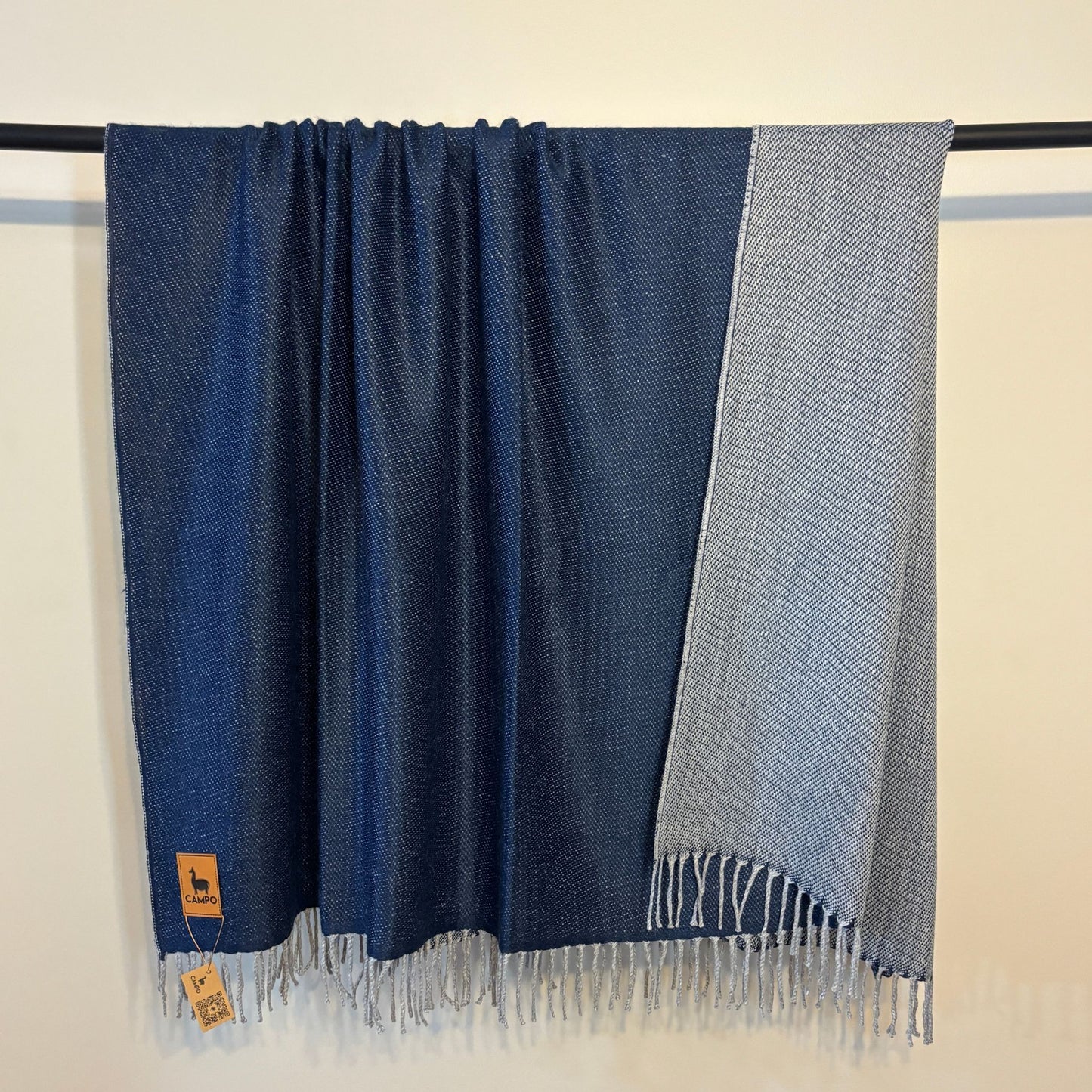 Blue and gray scarf with fringes on a black rod against a beige background