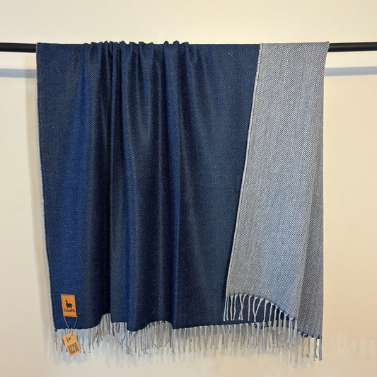 Blue and gray scarf with fringes on a black rod against a beige background