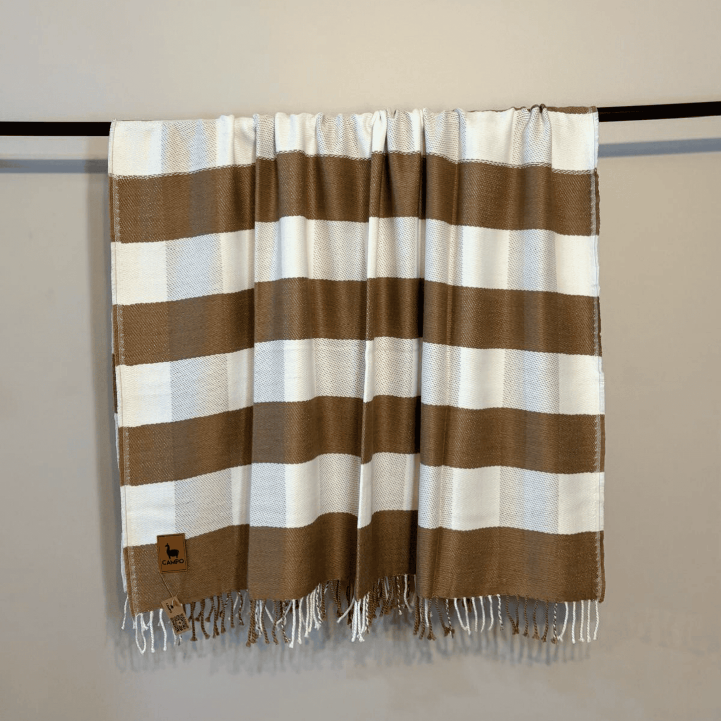 Striped brown and white blanket with fringes on a rack against a plain background