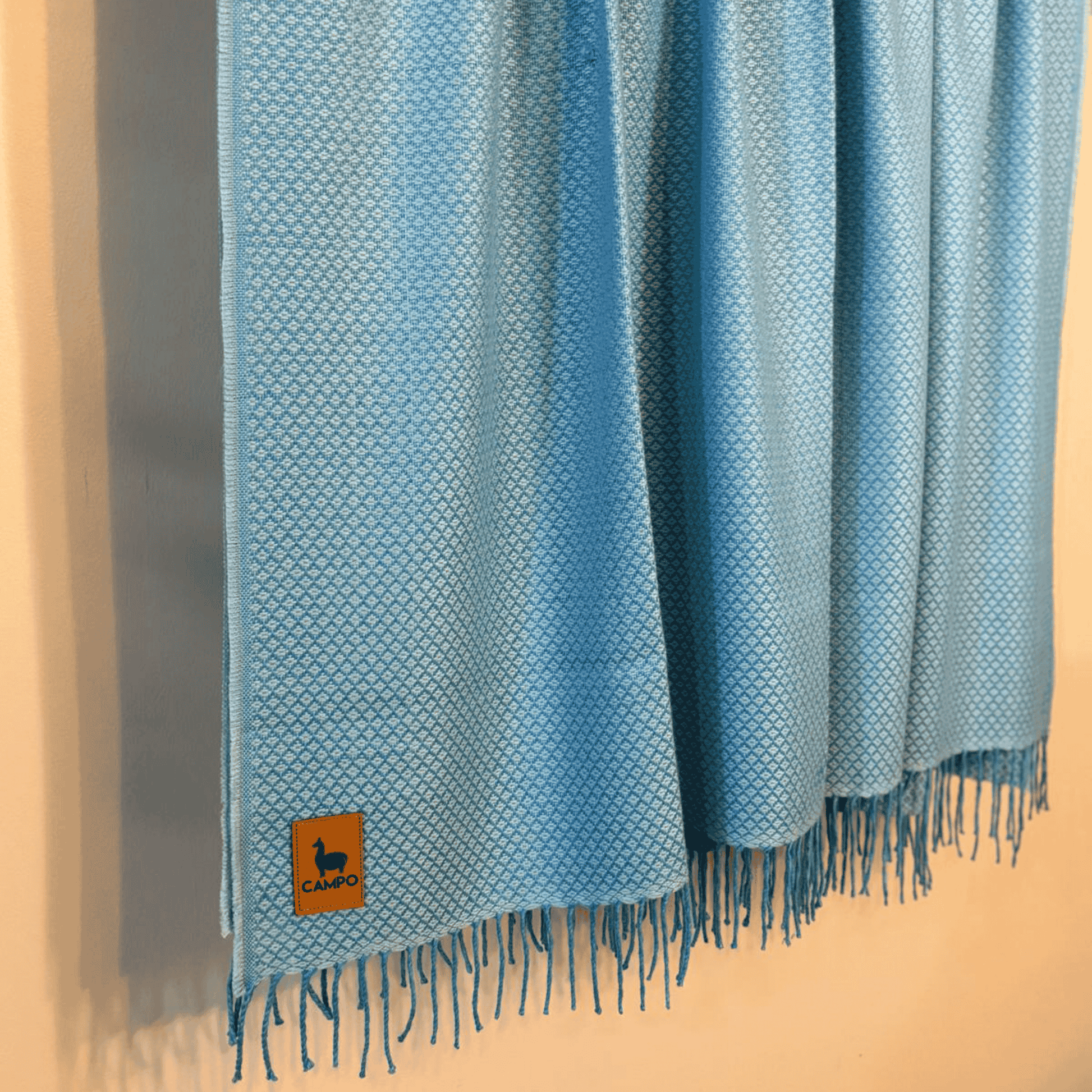 Blue woven blanket with fringes and a logo on a wooden surface