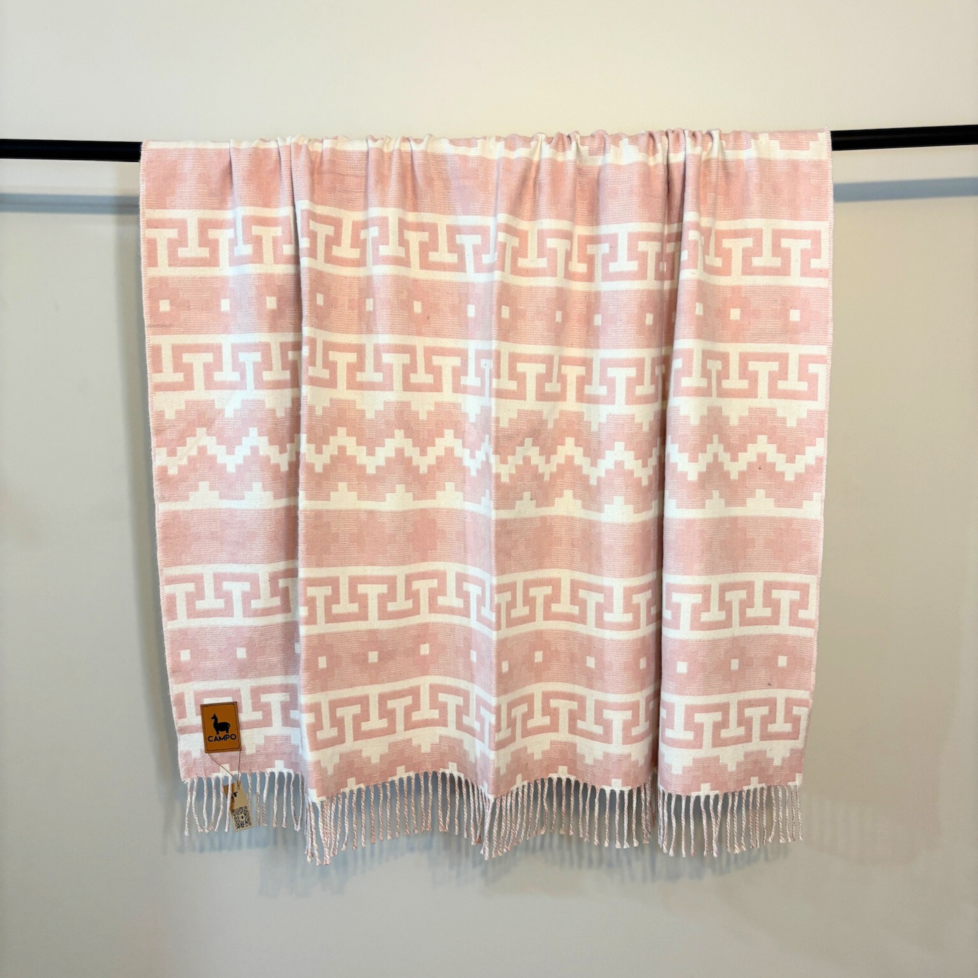 Blush pink and white patterned throw blanket on a rack against a white background