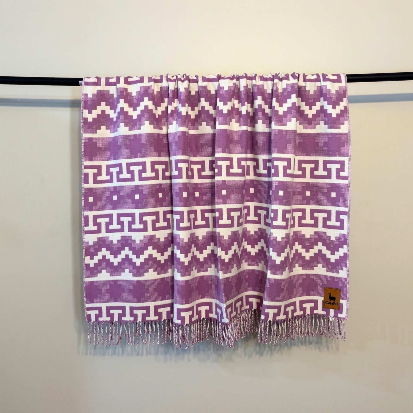 Fuchsia  patterned scarf with fringes on a rod against a plain background