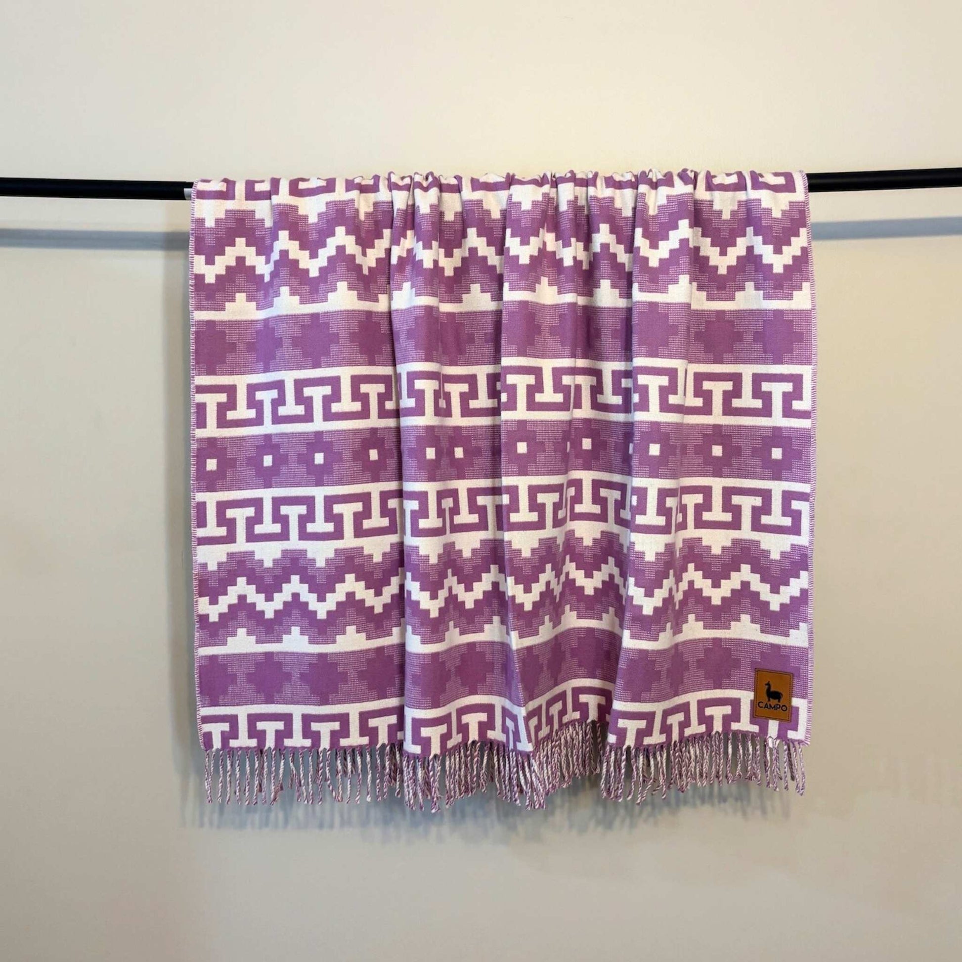 Fuchsia  patterned scarf with fringes on a rod against a plain background