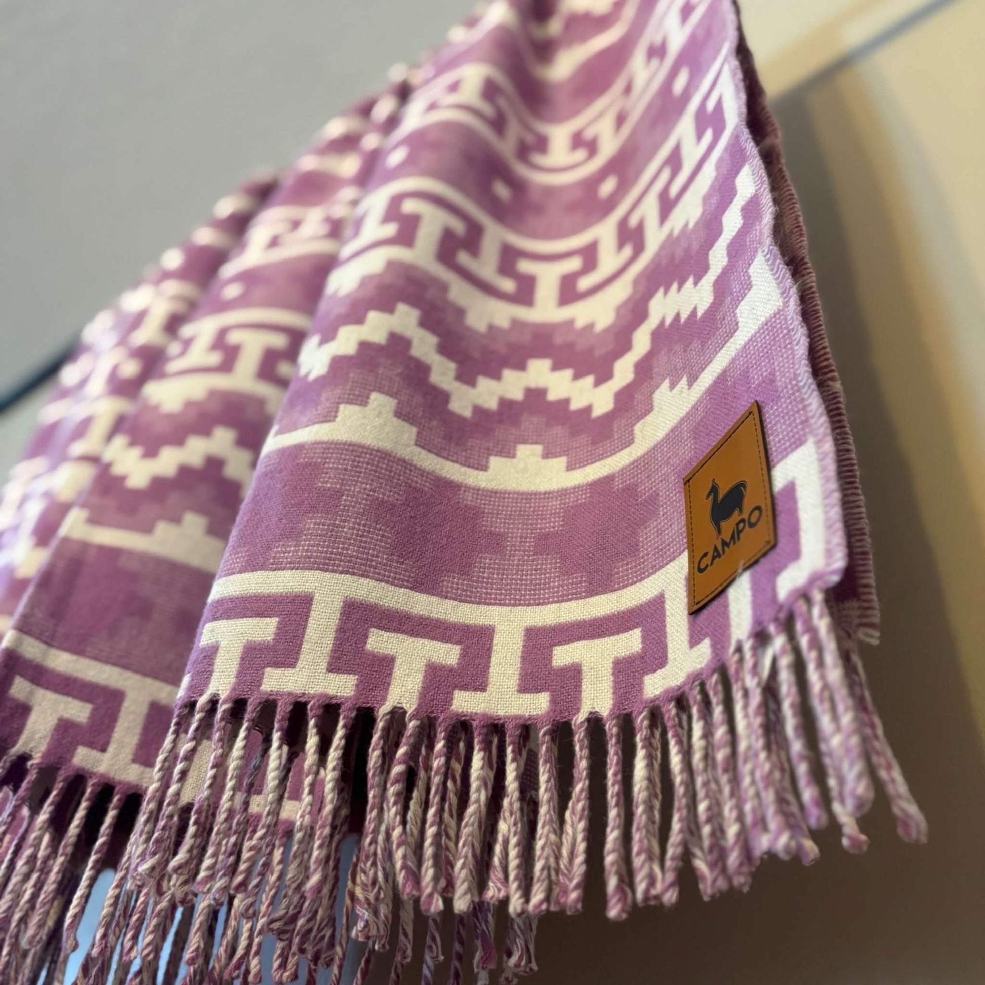 Fuchsia patterned scarf with fringes and a brand logo on a neutral background