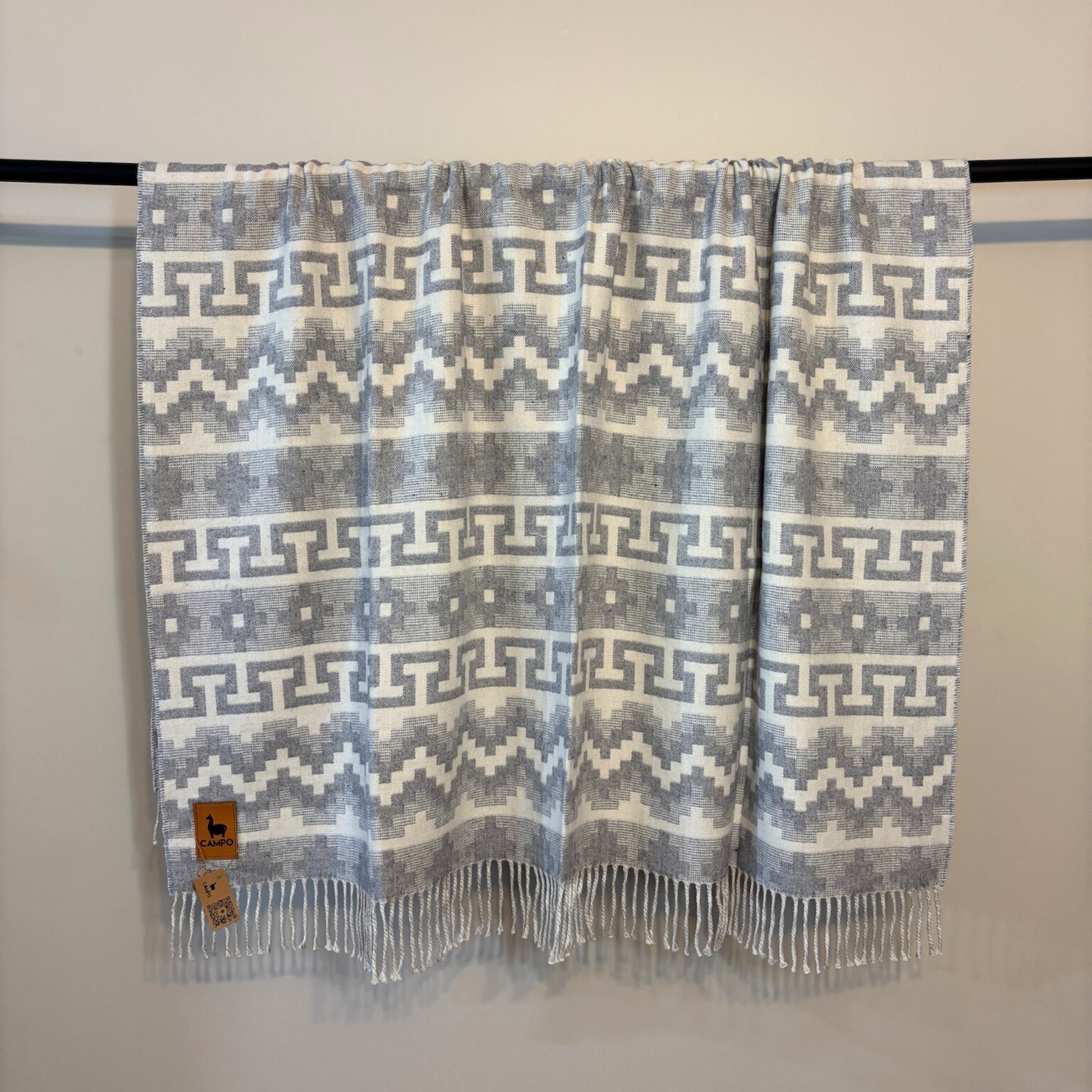Patterned blanket with fringes on a black rod against a white background