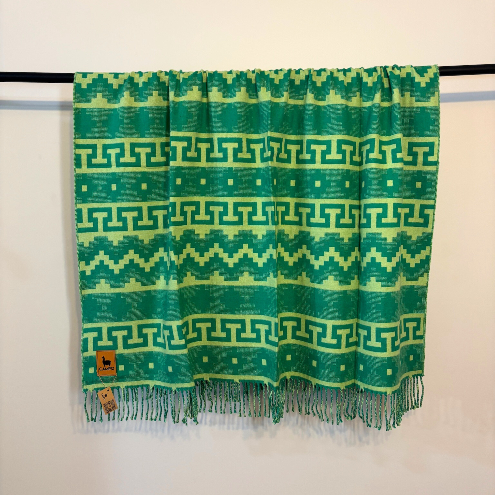 Green  patterned scarf with fringes on a black rod against a white background