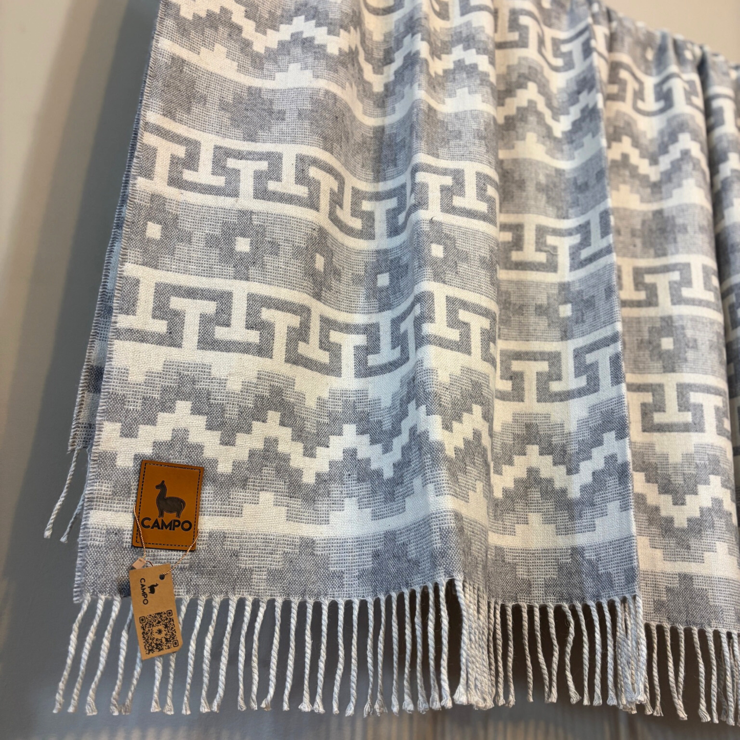 Gray and white patterned scarf with a brand tag on a neutral background