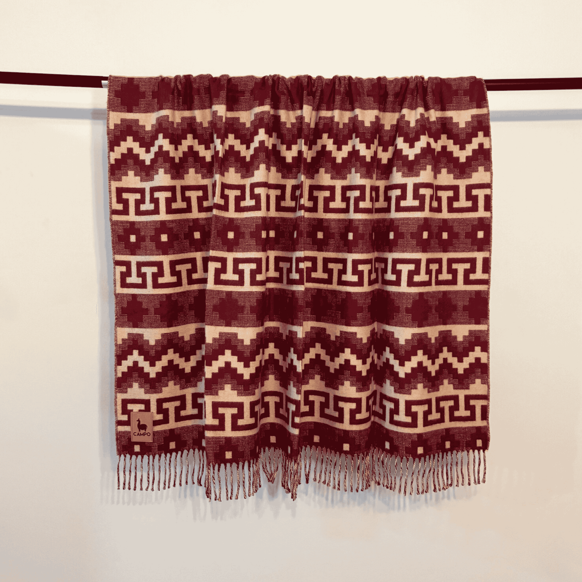 Woven blanket with geometric pattern and fringes on a wooden rod against a beige background