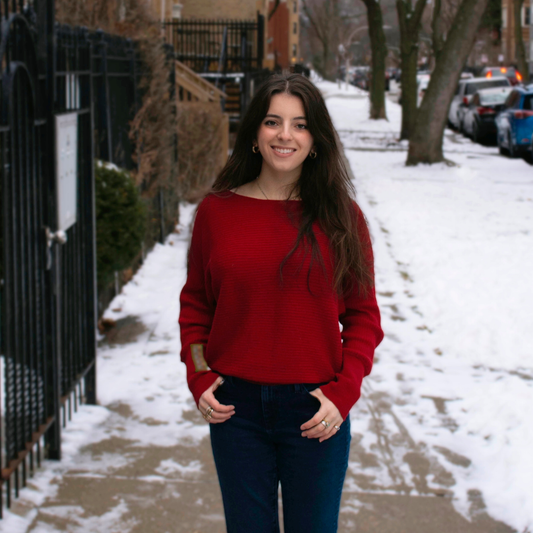 Woman in a red sweater standing on a snow-covered sidewalk.