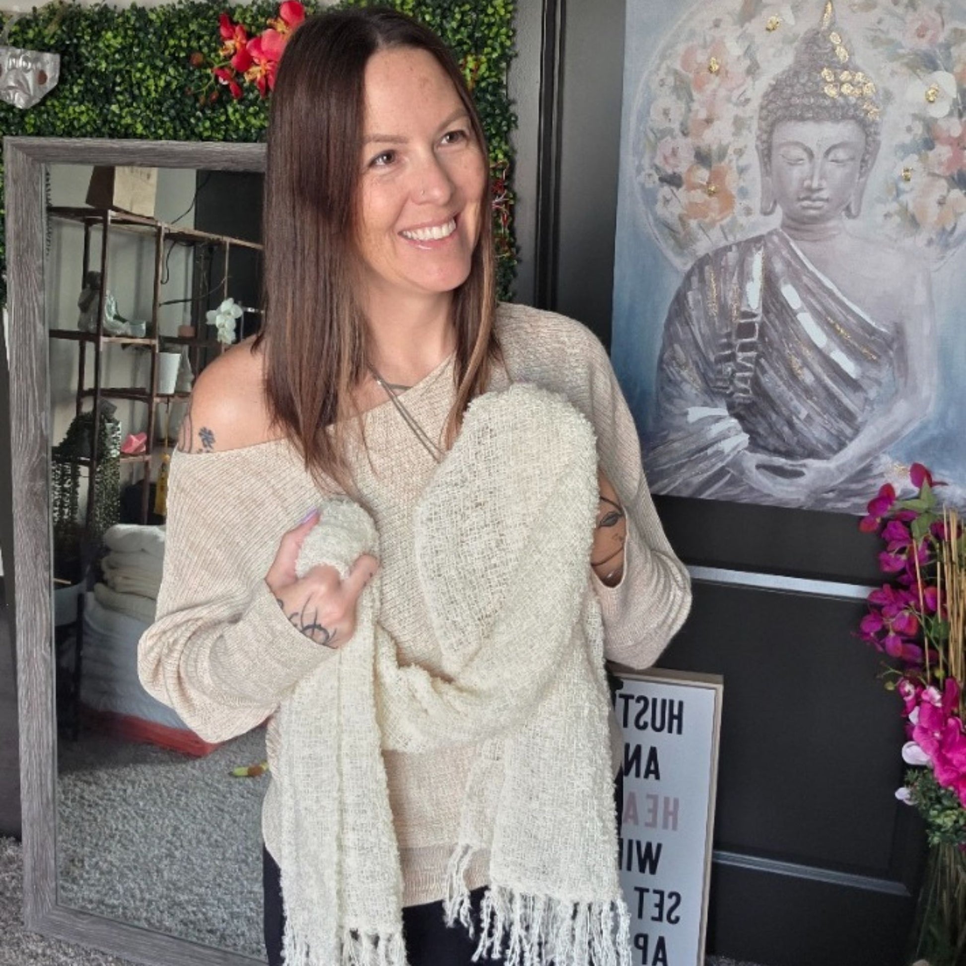 Woman holding a white scarf in a room with decor elements like a Buddha painting and plants.