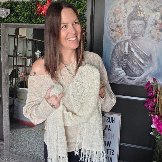 Woman holding a white scarf in a room with decor elements like a Buddha painting and plants.