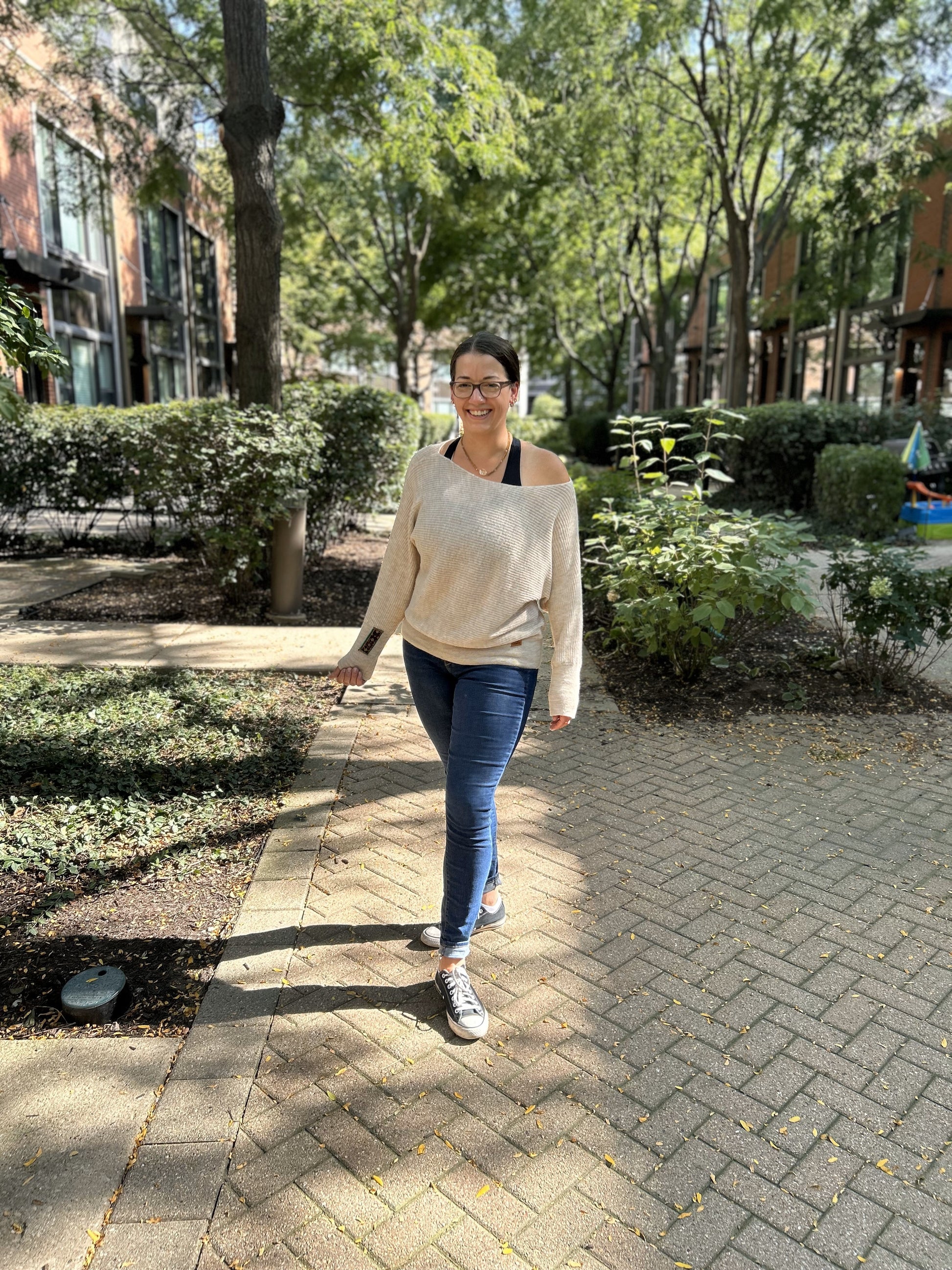 A person wearing an off-shoulder cream alpaca sweater walking on a brick pathway