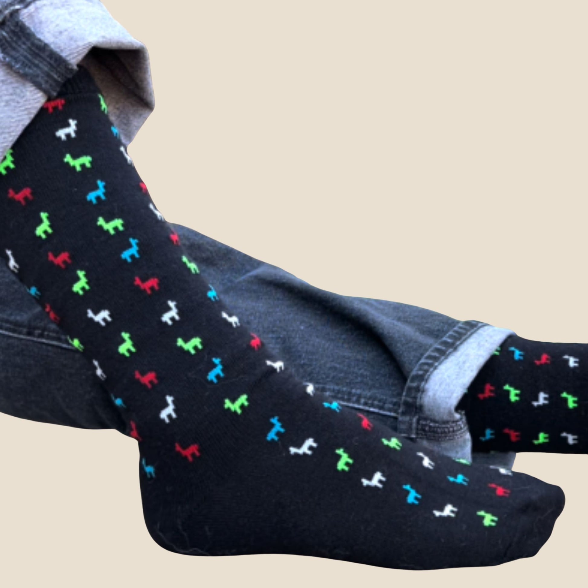 Black socks with colorful alpaca pattern worn with blue jeans on a beige background