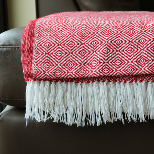 Red and white patterned blanket with fringes on a dark surface