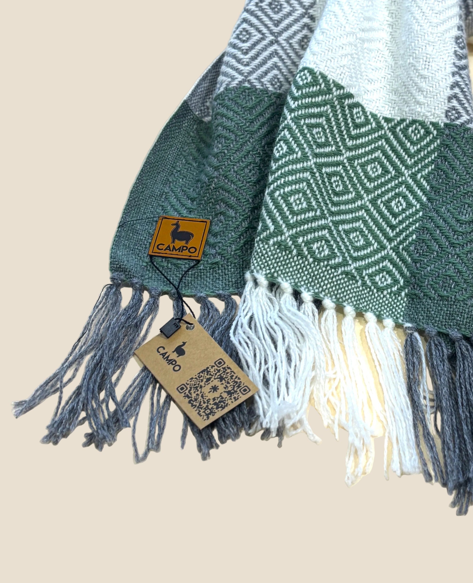 Green woven blanket with fringes and a visible brand tag on a light background