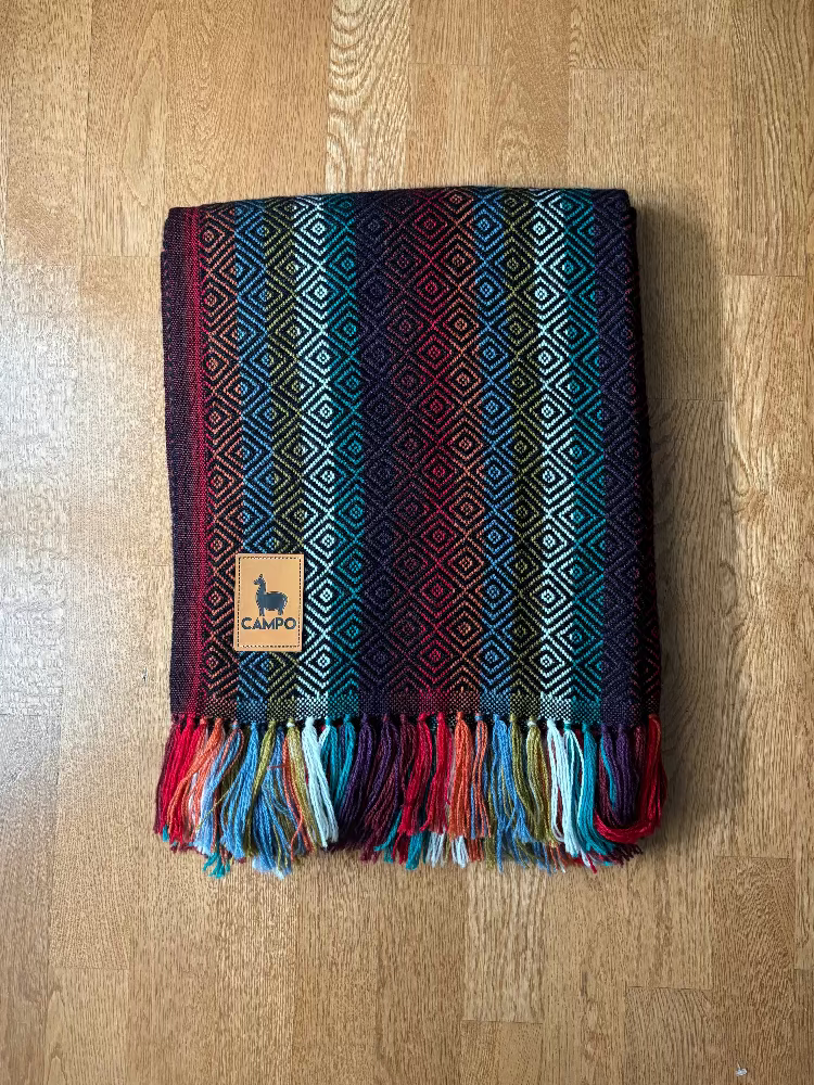 Colorful woven alpaca blanket with fringes on a wooden surface