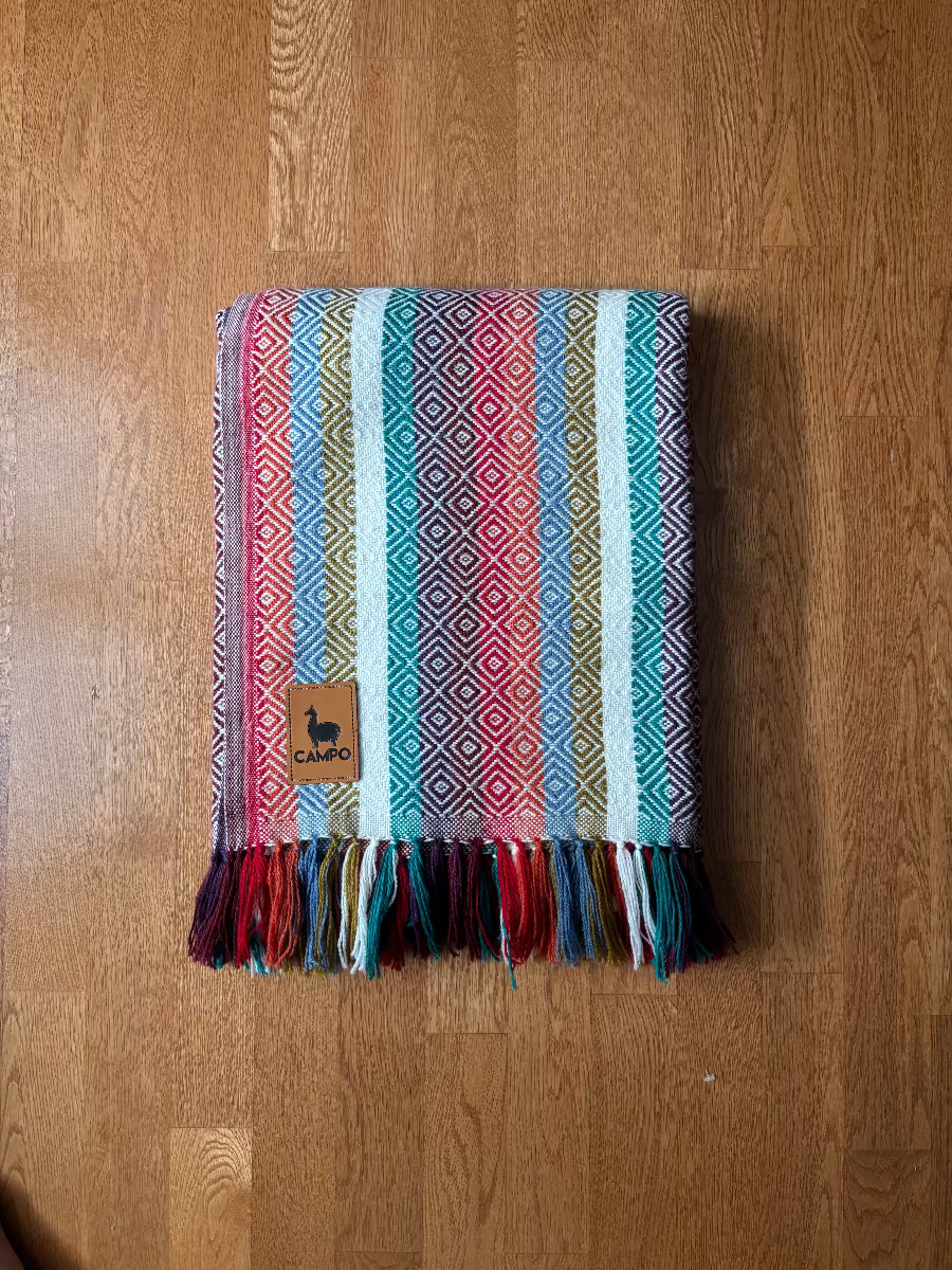 Colorful striped alpaca blanket with tassels on a wooden floor - Peruvian Designs