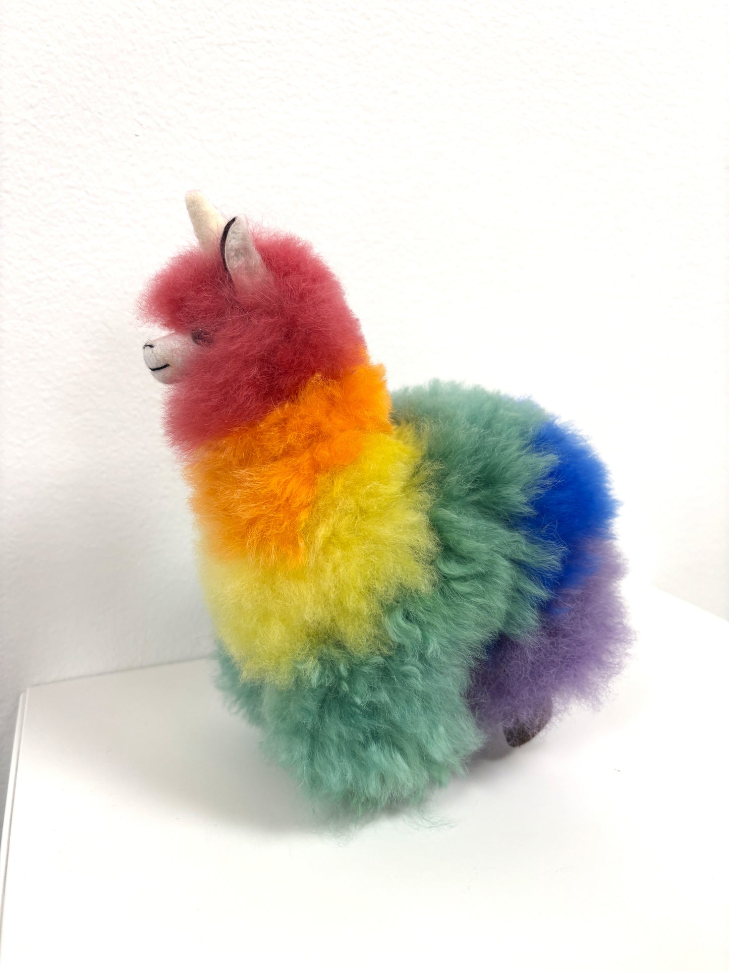 Colorful plush toy resembling a llama with a unicorn horn on a white background