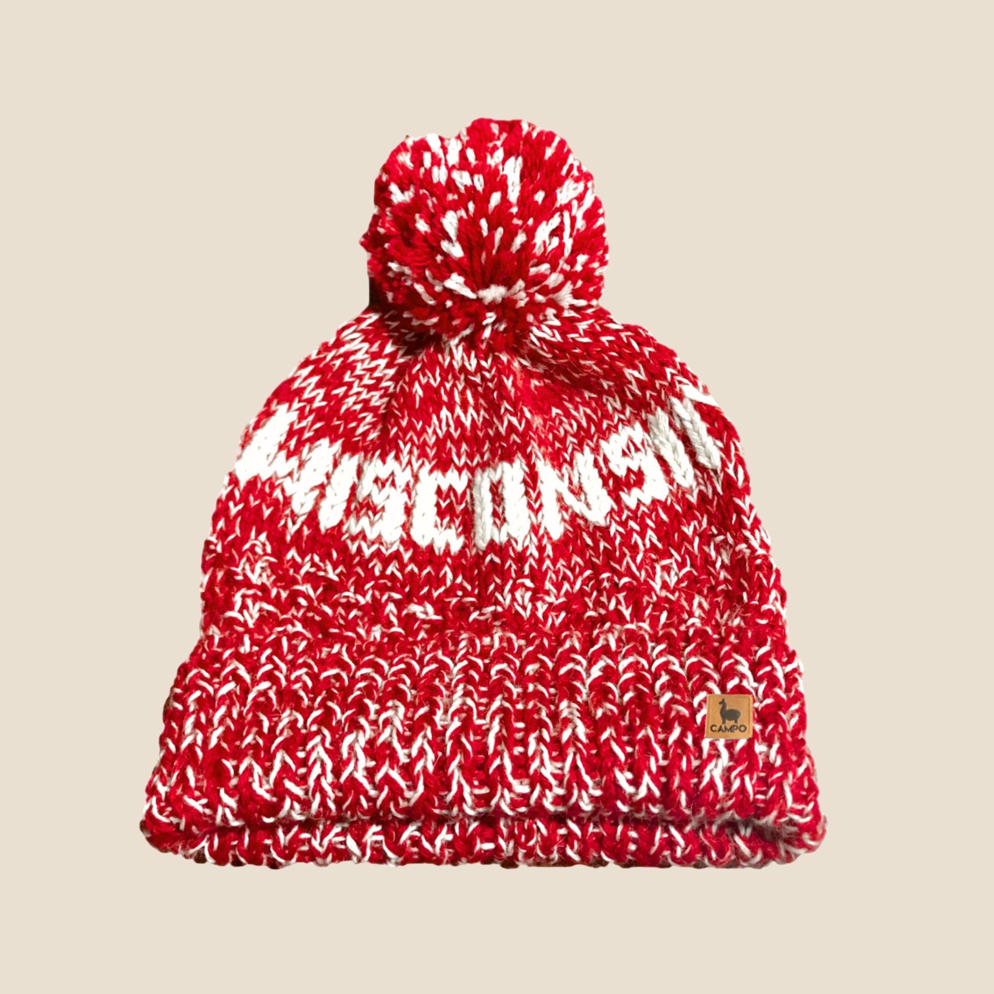 Red and white knit beanie with pom-pom on a beige background