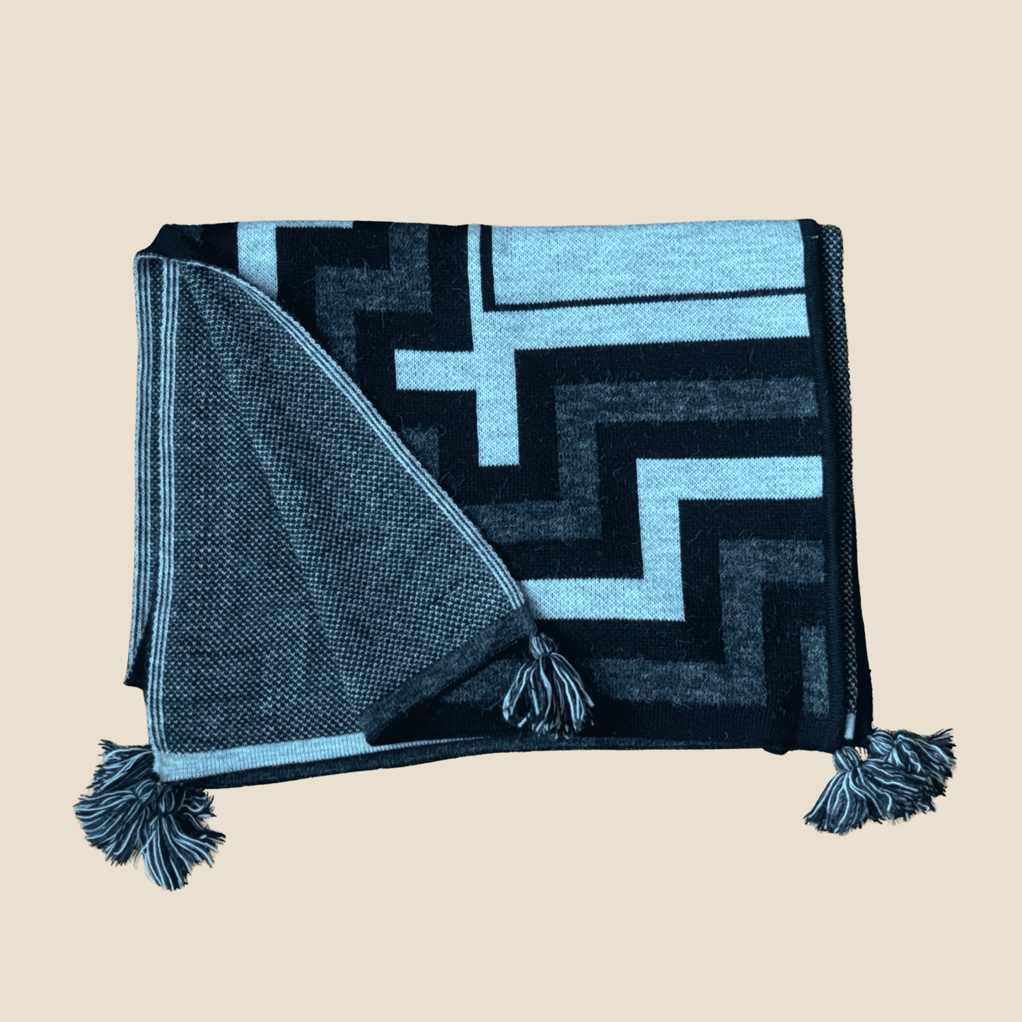 Black and blue patterned throw blanket with tassels on a beige background