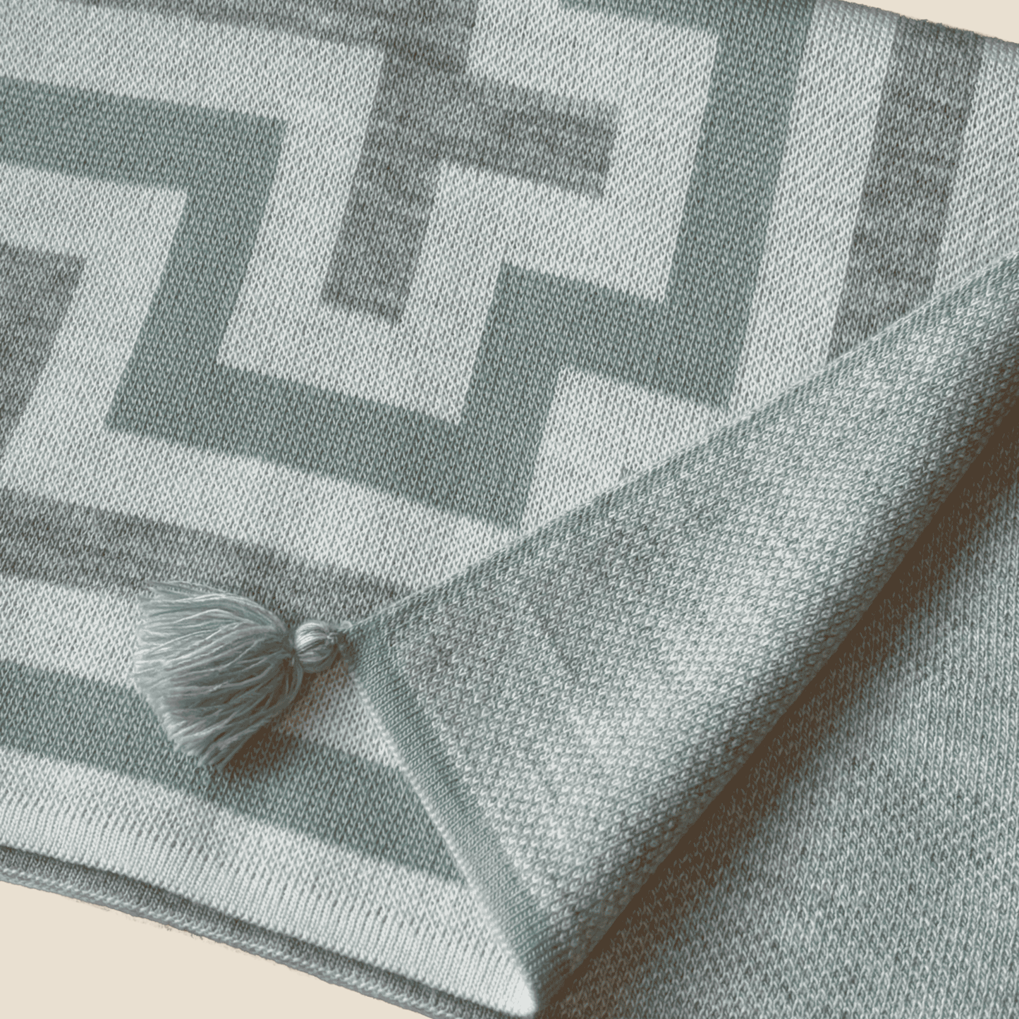 Gray and white geometric patterned blanket with a tassel on a beige background