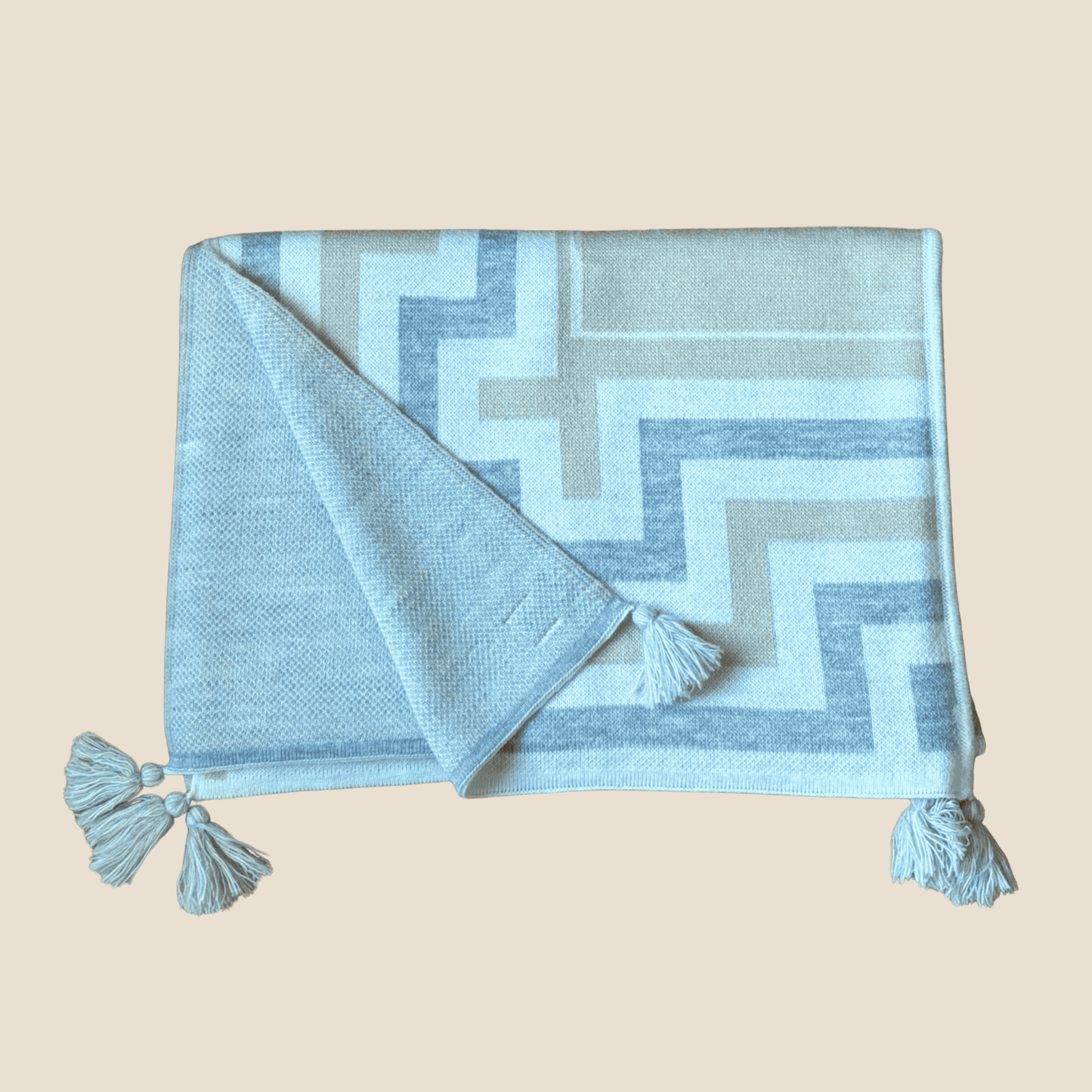 Light blue and gray patterned blanket with tassels on a beige background