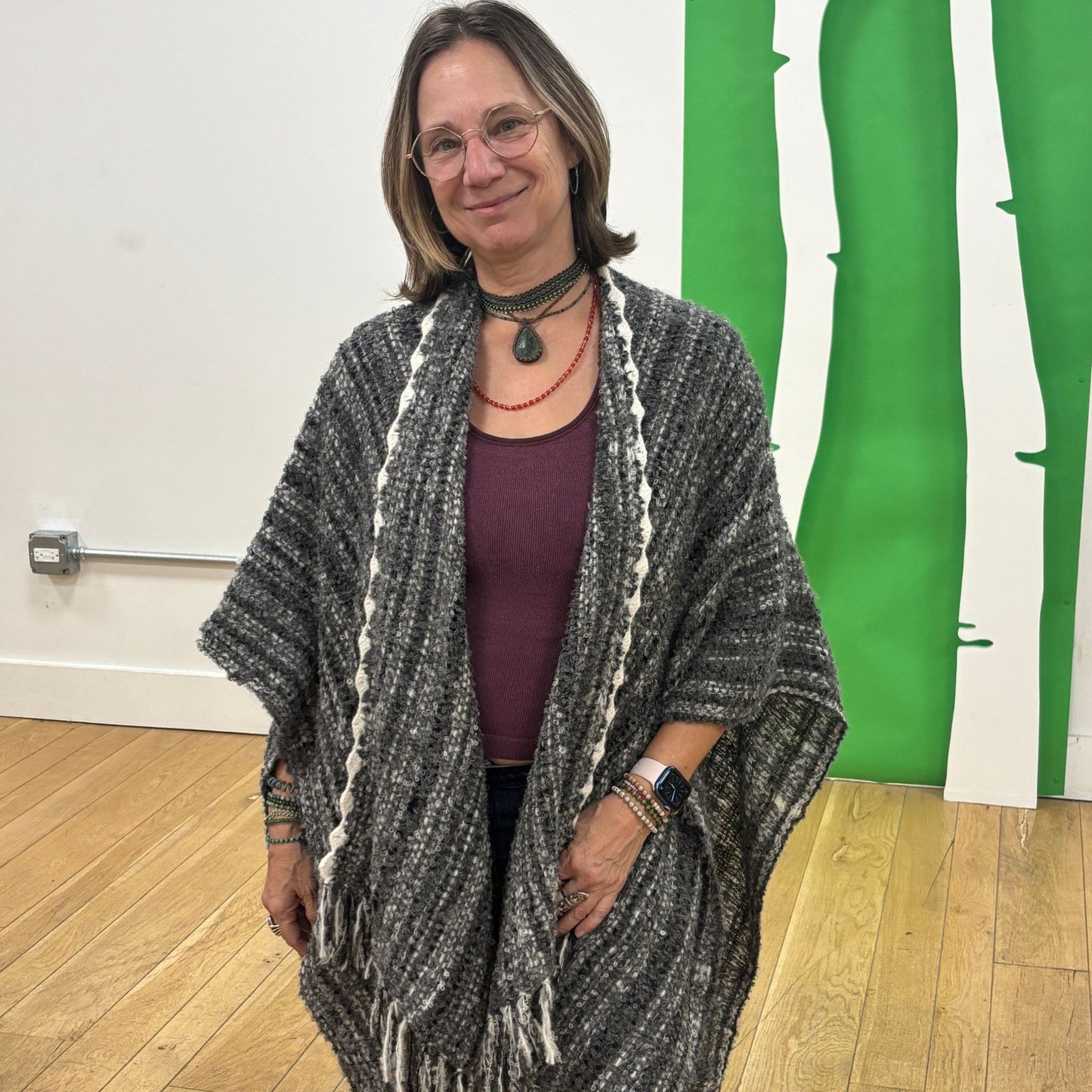 Woman wearing a gray shawl over a purple top in an indoor setting with green vertical elements on the wall.