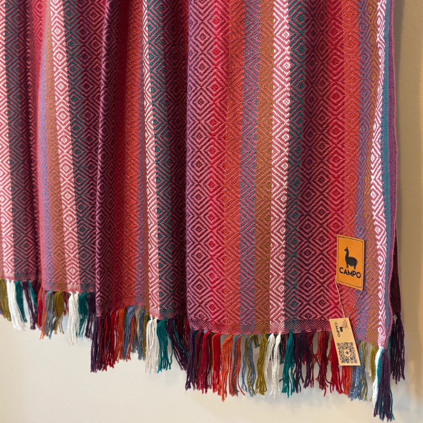 Pink woven blanket with fringes and a visible brand tag on a neutral background