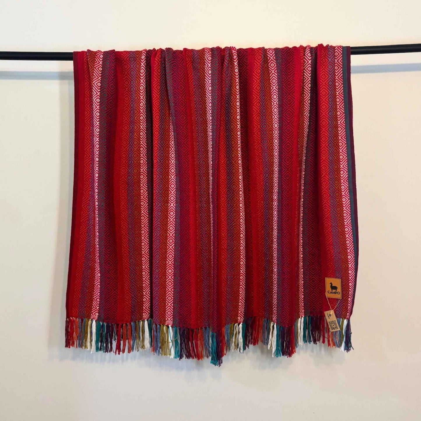 Red striped blanket with fringes on a black rod against a white wall