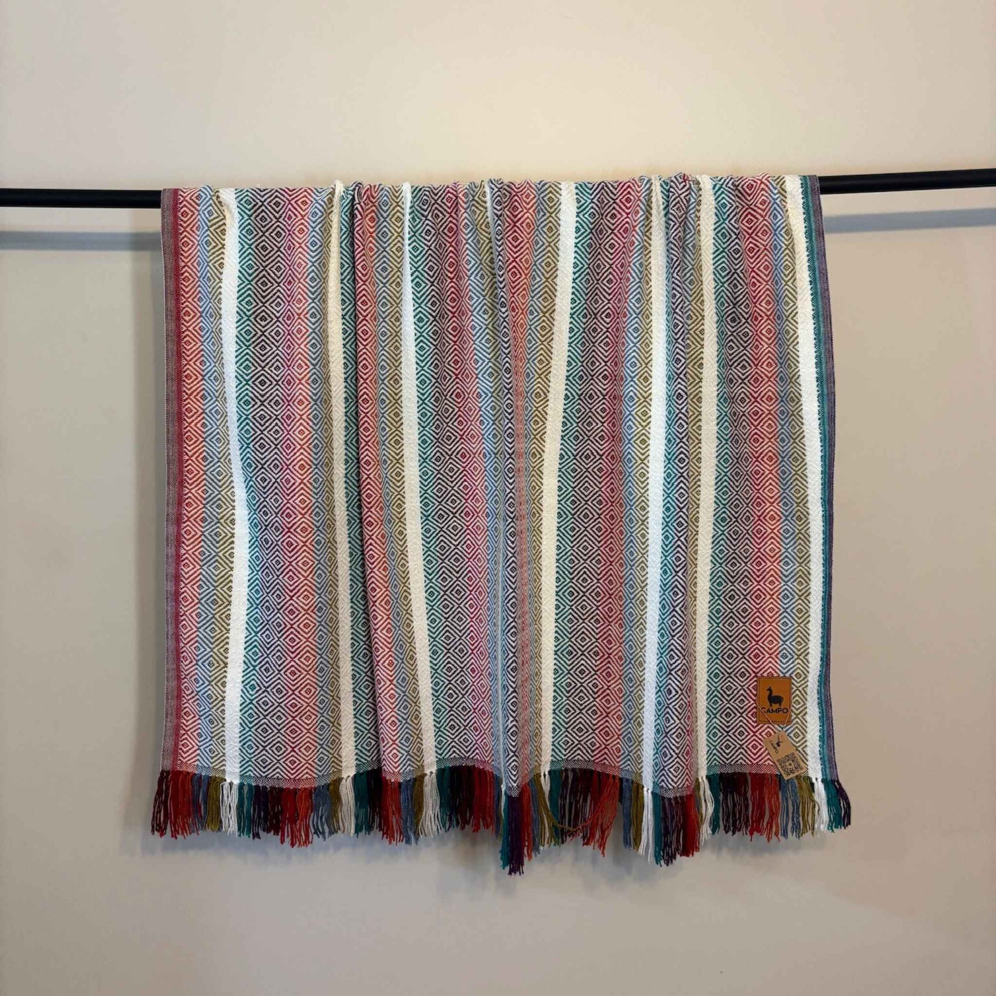 White multi striped scarf with fringe hanging on a rack against a white wall.