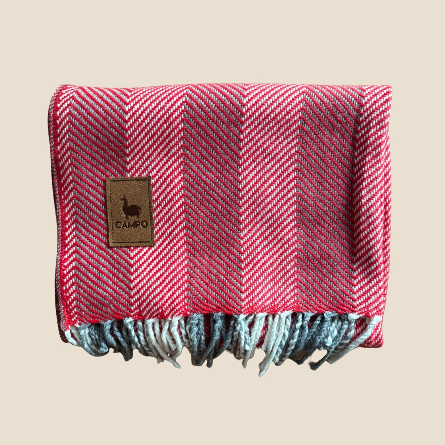 Red and gray herringbone patterned blanket with a brand label on a beige background