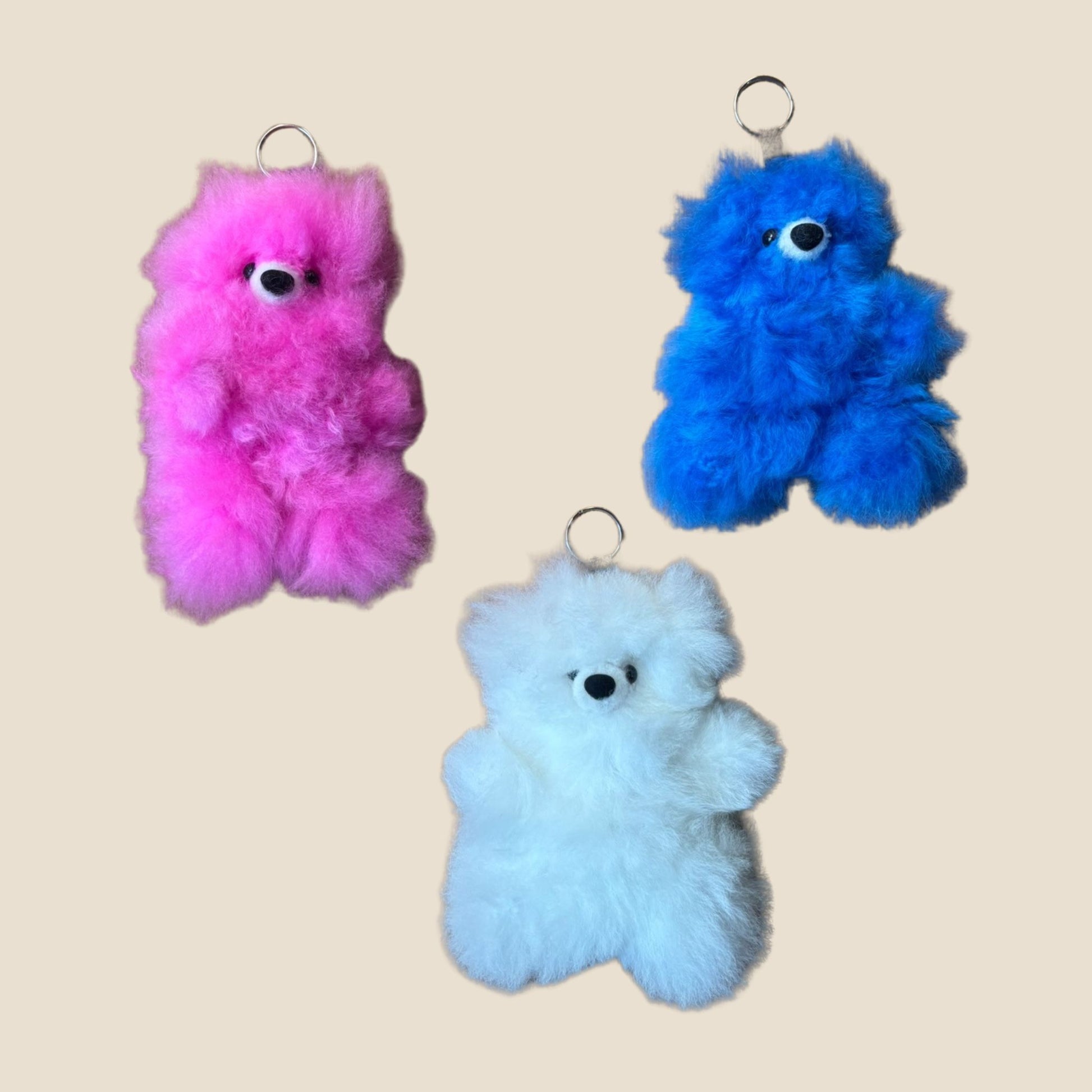Three colorful plush keychains shaped like bears on a beige background