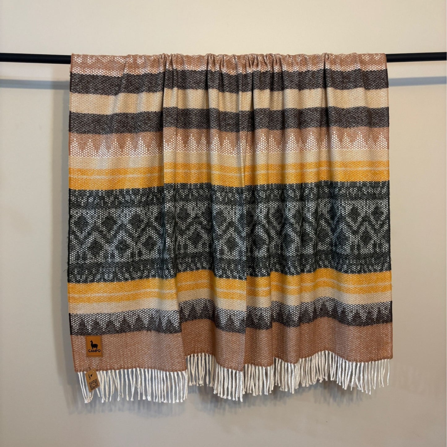 Green medley striped patterned blanket with fringes on a black rod against a beige wall