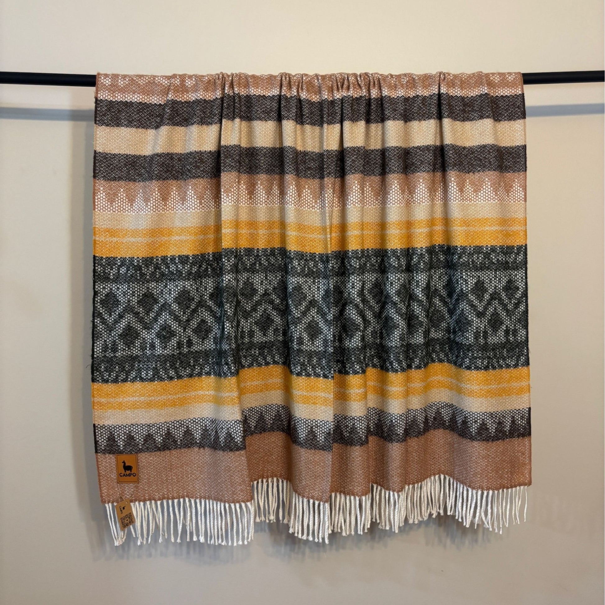 Green medley striped patterned blanket with fringes on a black rod against a beige wall