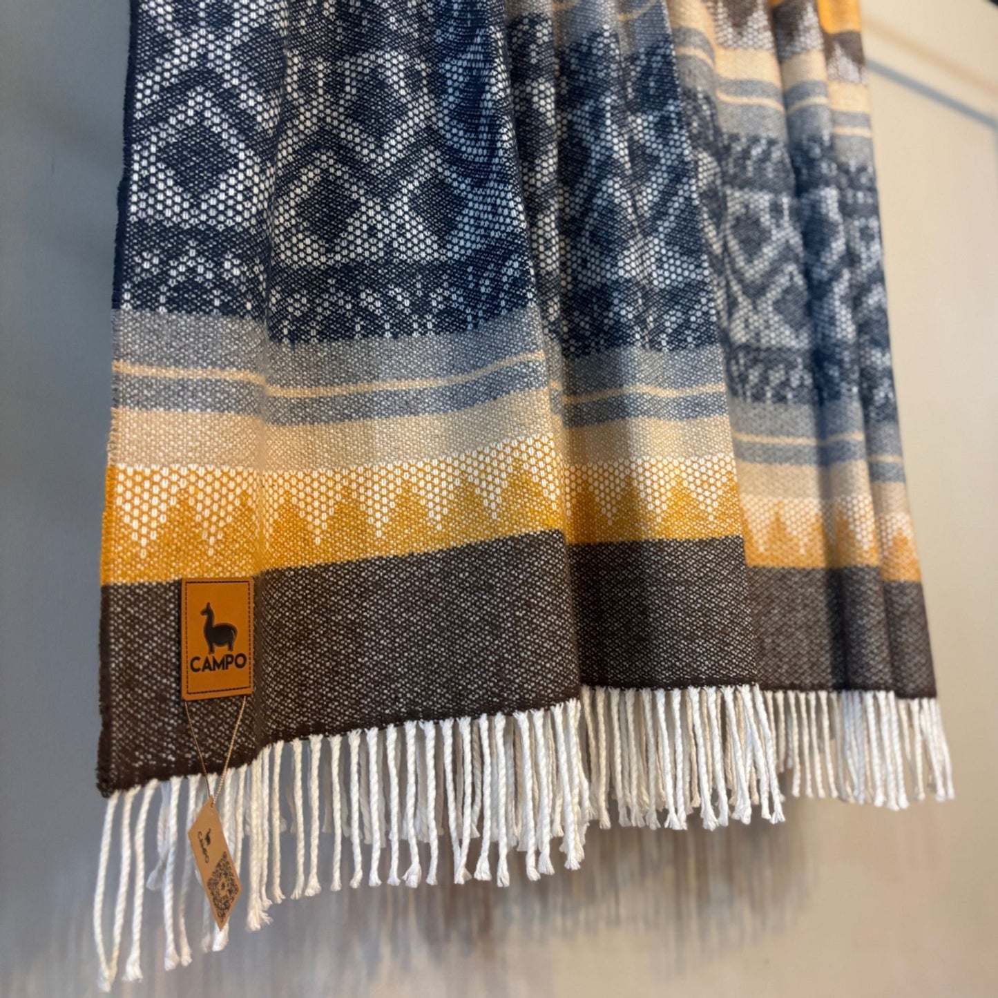 Dark blue medley woven fabric with geometric pattern and fringes, featuring a visible brand label.