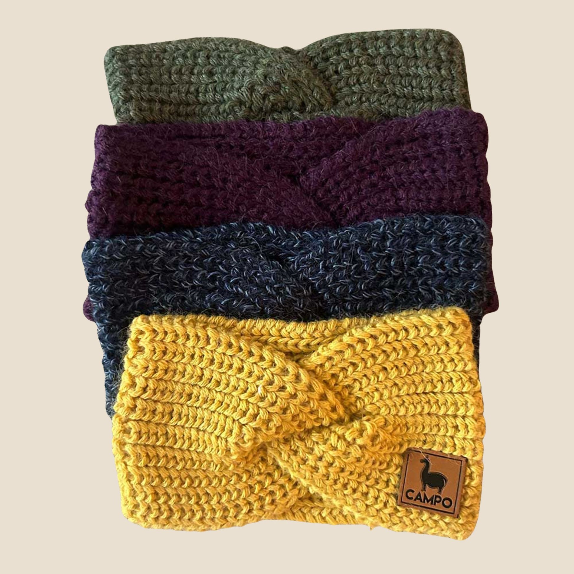 Stack of twisted headbands in green, purple, blue, and yellow with a visible brand label on a beige background.