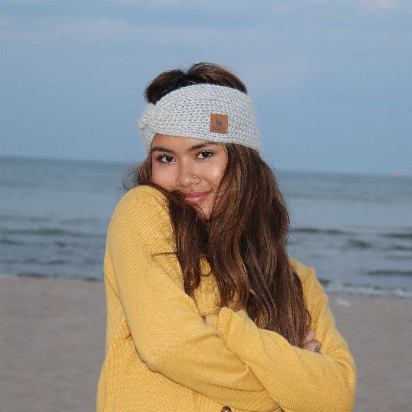 Woman wearing a white knitted headband with a logo on a beach
