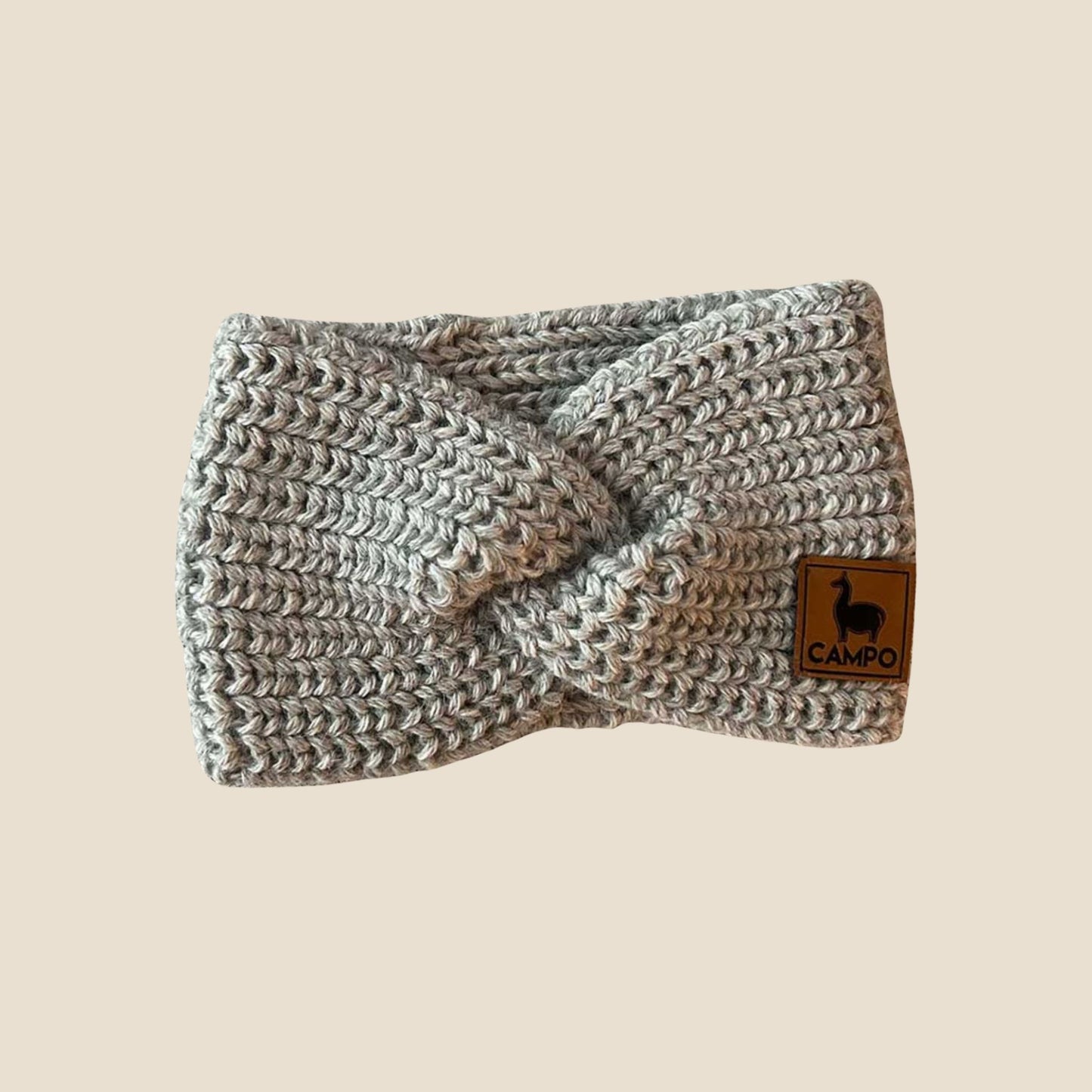 Light gray twisted headband with a brand label on a beige background
