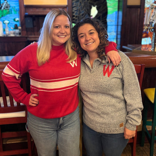 Two women wearing red and gray sweatshirts with a letter 'W' in a casual setting.