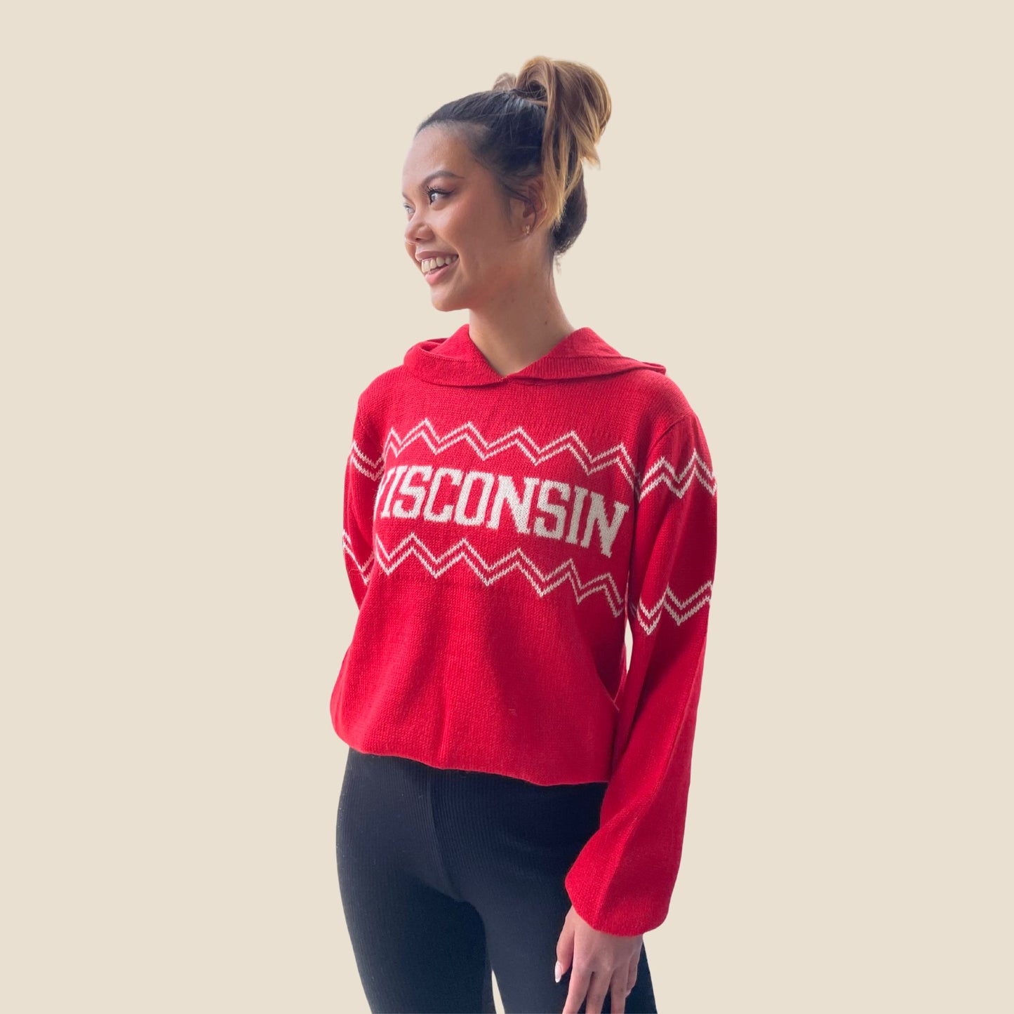 Person wearing a red 'Wisconsin' sweater on a beige background