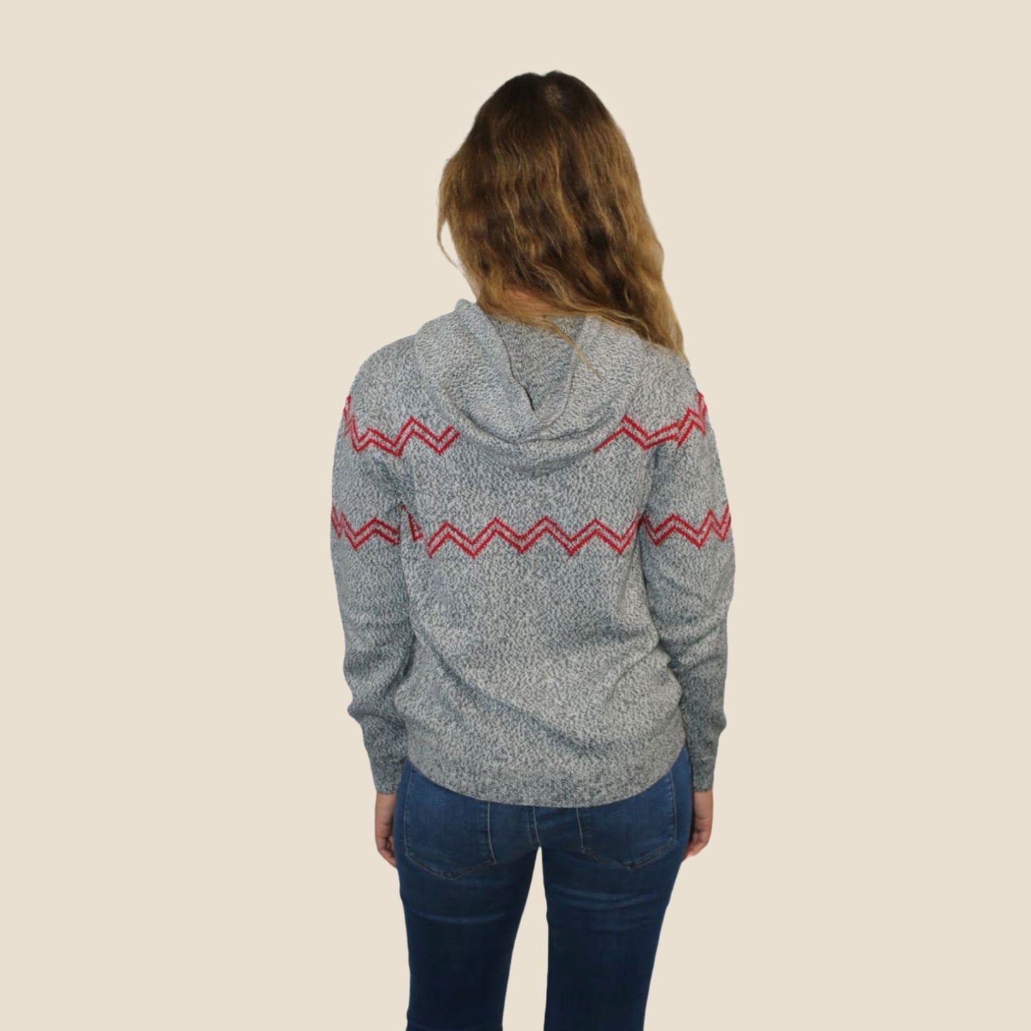 Person wearing a gray hoodie with red zigzag pattern on the back, standing against a beige background