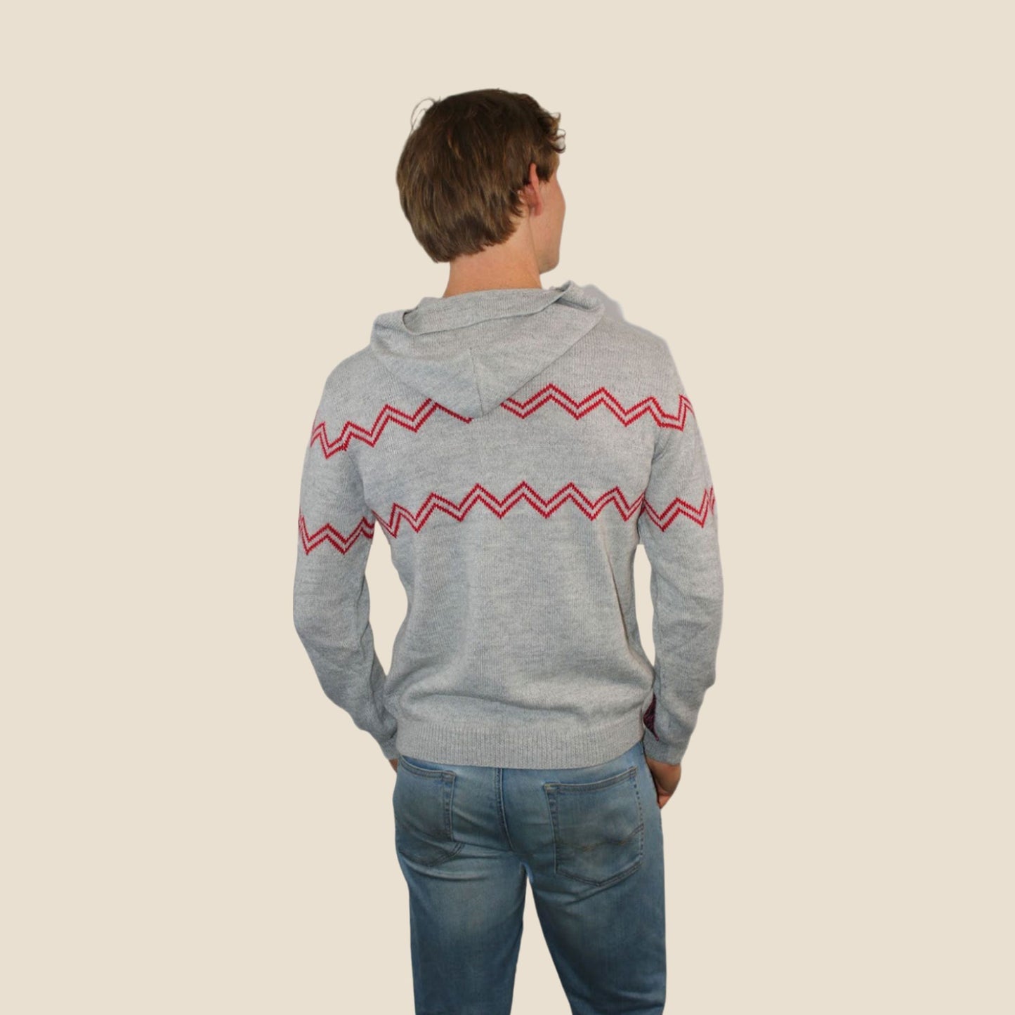 Person wearing a gray hoodie with red zigzag pattern on the back, standing against a beige background