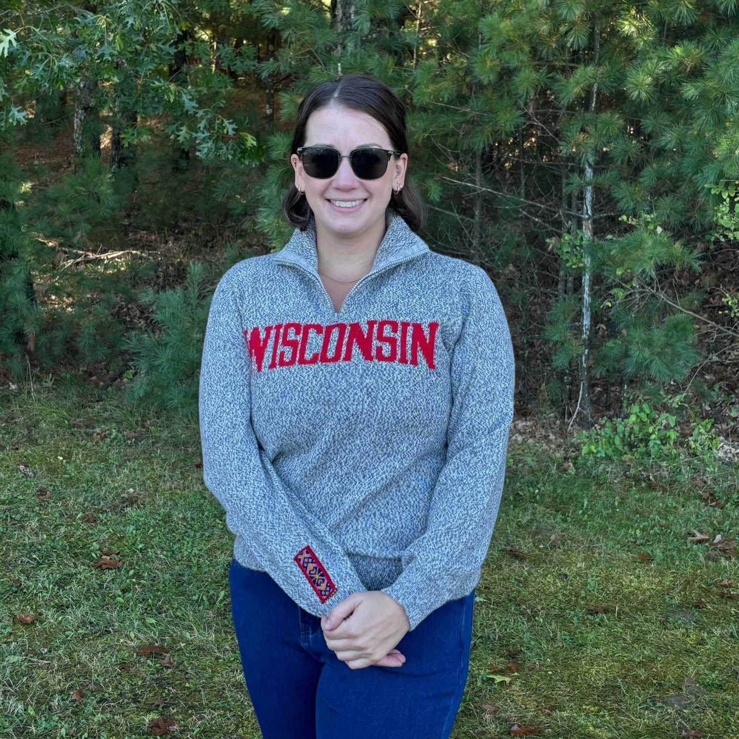 Person wearing a gray 'Wisconsin' sweater standing outdoors with trees in the background