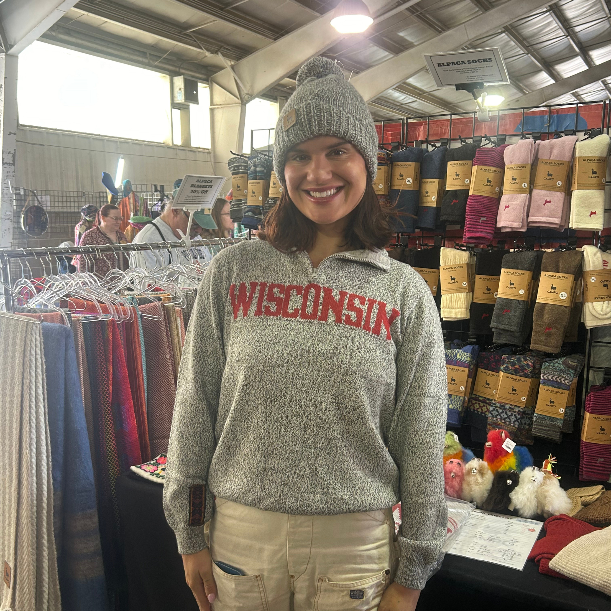 Woman wearing a 'Wisconsin' sweatshirt in a store with clothing racks and merchandise.