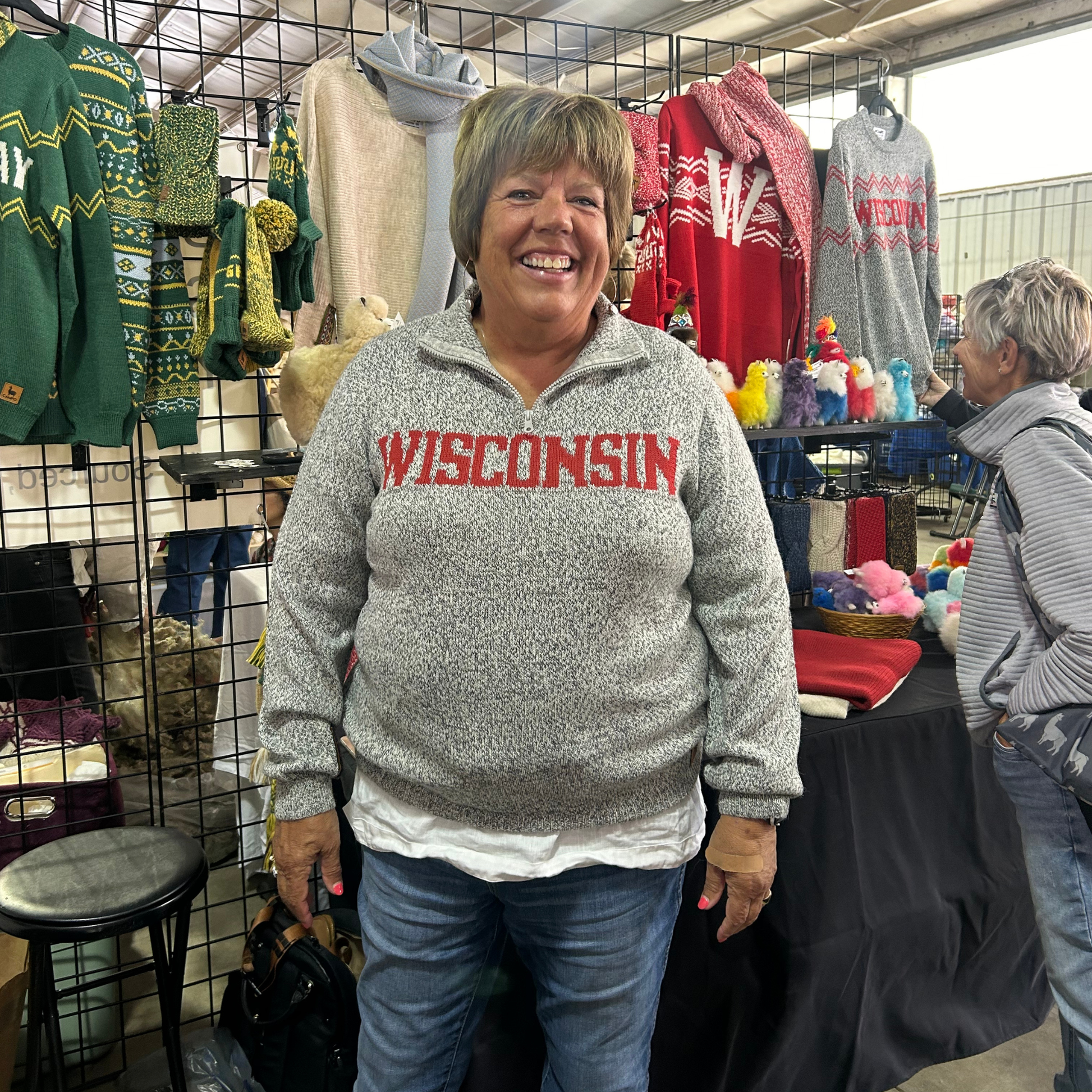 Woman wearing a 'Wisconsin' sweatshirt in a market setting with various items on display.