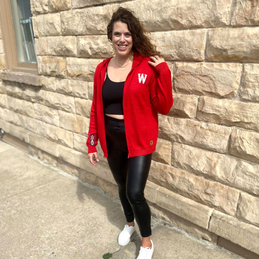 Woman wearing a red jacket with a white letter 'W' standing against a stone wall.