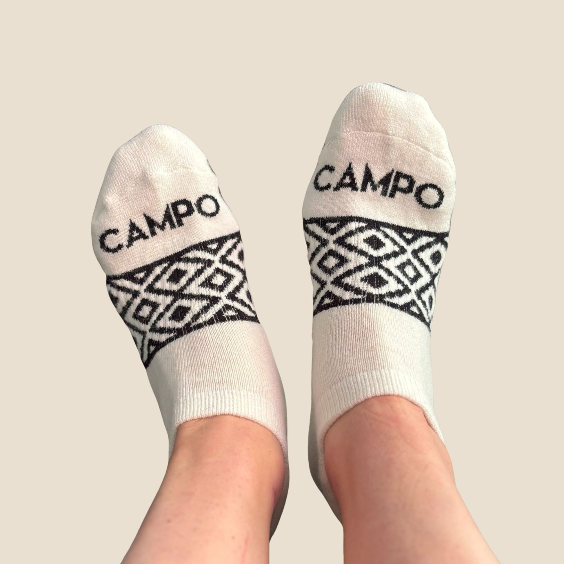 White socks with black geometric patterns and 'CAMPO' branding on a beige background
