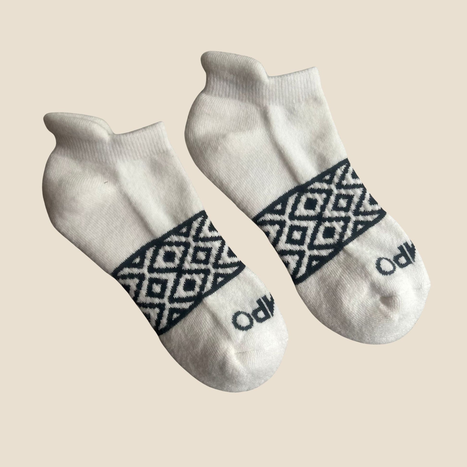 Pair of white socks with black geometric pattern on a beige background
