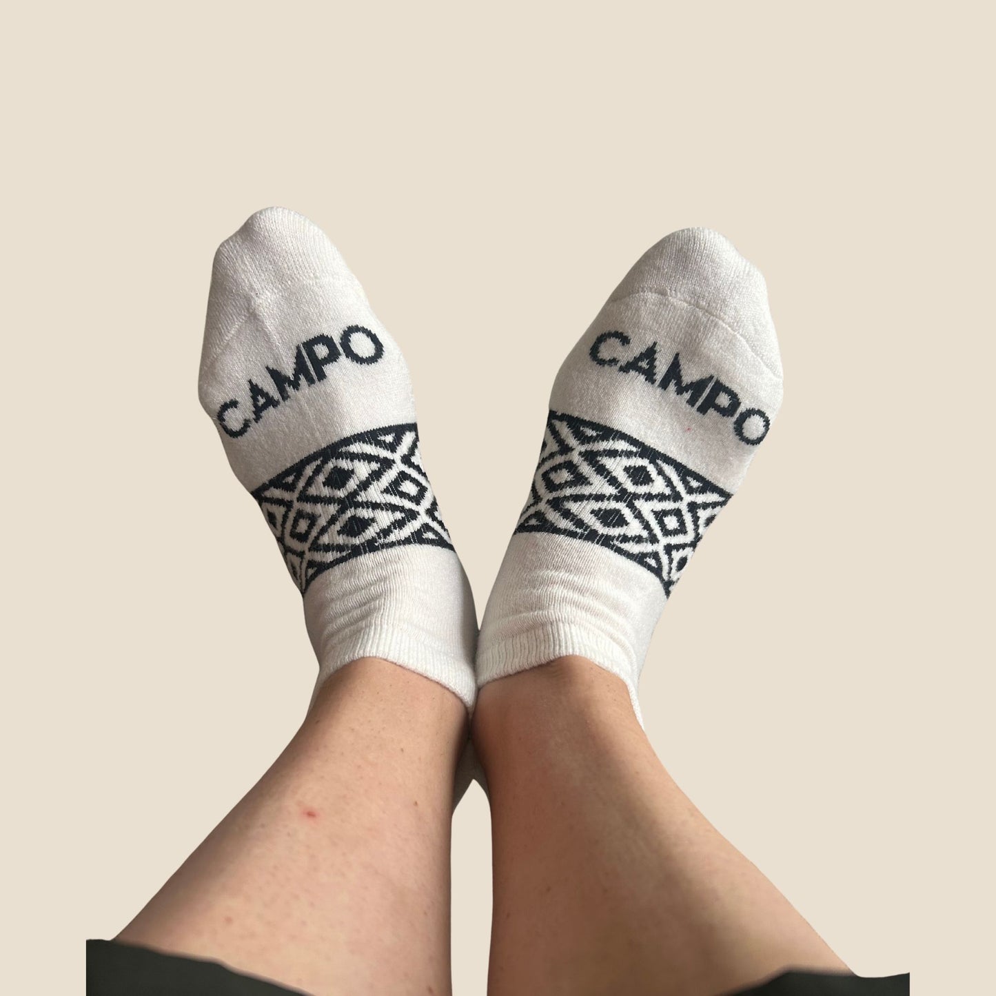 White socks with black patterns and 'CAMPO' branding on a beige background